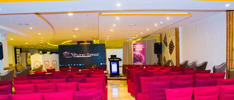 Un salón de conferencias con hileras de sillas rojas, un escenario con un cartel de 'Pure Spot' y un sistema de sonido.