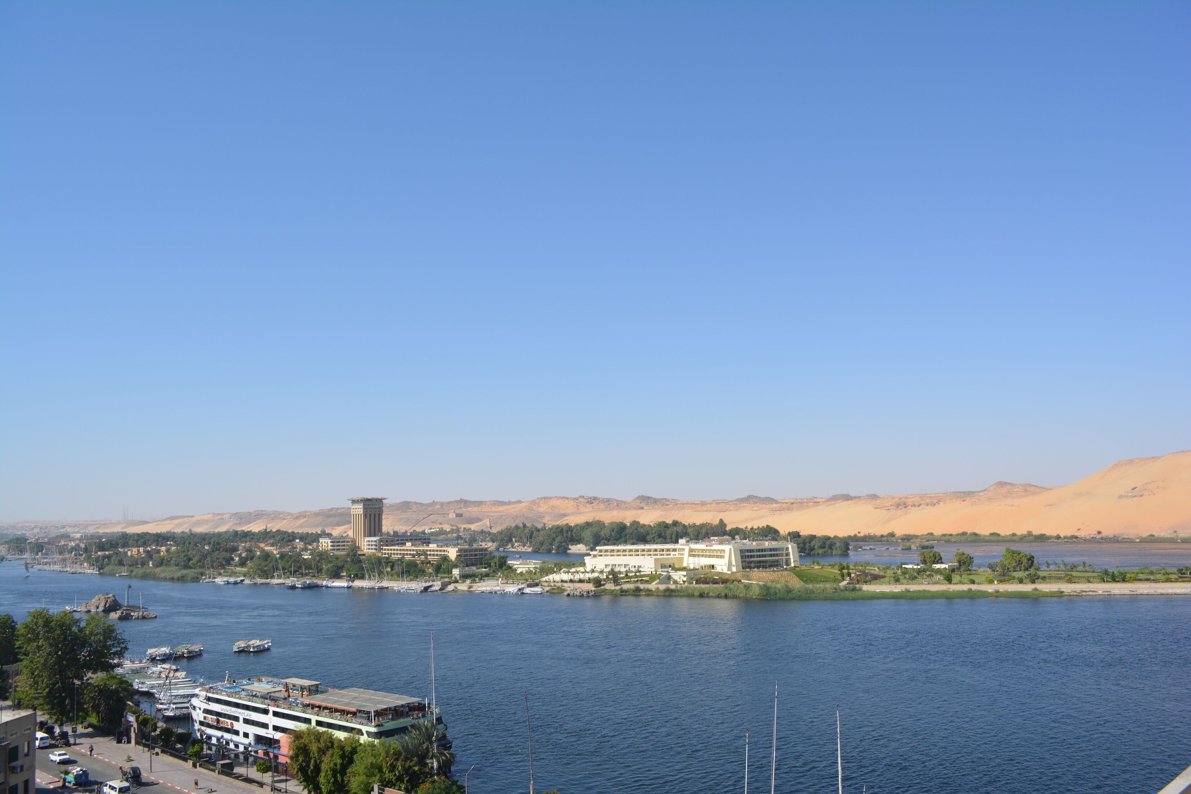 Un río con edificios a lo largo de sus orillas, cielo despejado y colinas al fondo.