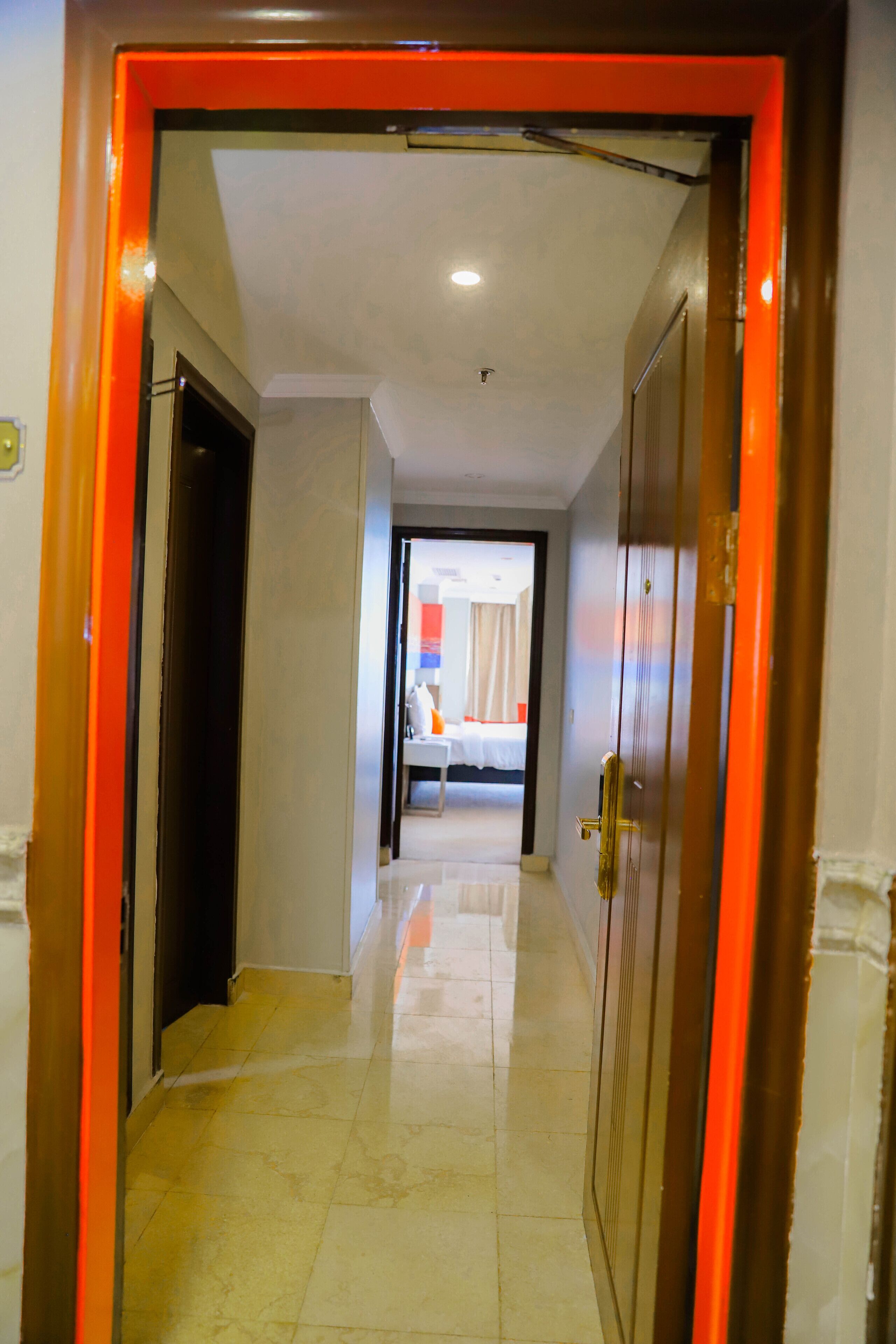 A hallway leading to a bedroom with a bed, a nightstand, and a window.