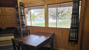 A wooden-paneled room with a dining table and chairs, a sofa, and a window with curtains. - Galeria In The Garden (Plovdiv)