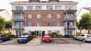 A multi-story residential building with a central entrance, balconies on each floor, and a parking area in front. - Ferncourt (Dublin)