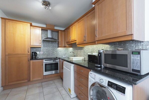 A kitchen with wooden cabinets, a dishwasher, a washing machine, a stove, and a microwave.