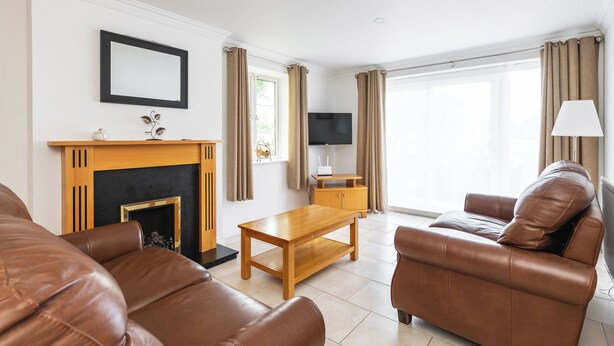 A living room with a fireplace, leather sofas, a wooden coffee table, a TV, and a lamp. - Ferncourt (Dublin)