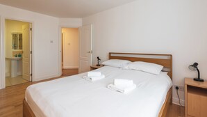 A neatly made bed with white linens and towels, a wooden headboard, a bedside table with a lamp, and a bathroom visible through an open door. - Ferncourt (Dublin)