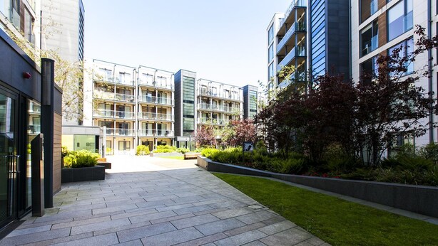 Une cour intérieure urbaine moderne, dotée d’une allée pavée et entourée d’immeubles à plusieurs étages, avec des balcons et de grandes fenêtres.