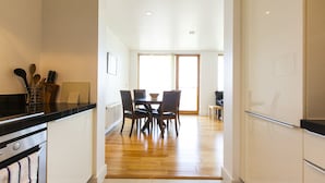 Une cuisine avec un plancher en bois, un coin repas avec une table et des chaises, et une vue sur l’extérieur grâce à une grande fenêtre.