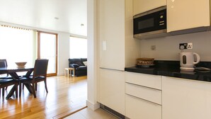 Une cuisine moderne avec des armoires blanches, un comptoir noir et un four à micro-ondes. On aperçoit un coin repas avec une table et des chaises à l’arrière-plan.
