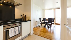 Une cuisine moderne dotée d’un four et d’une cuisinière encastrés, un coin repas avec une table et des chaises, et une grande fenêtre qui laisse entrer la lumière naturelle.