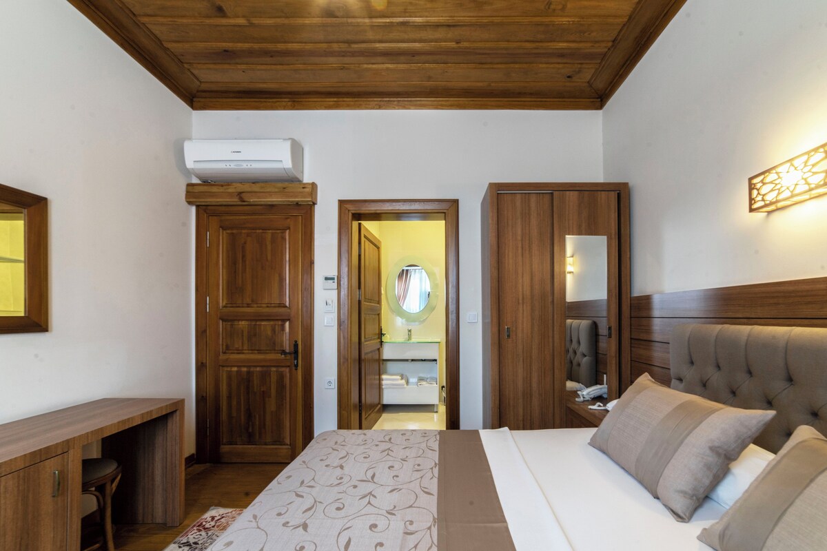 A bedroom with a bed, a desk, a wardrobe, and a bathroom visible through an open door.
