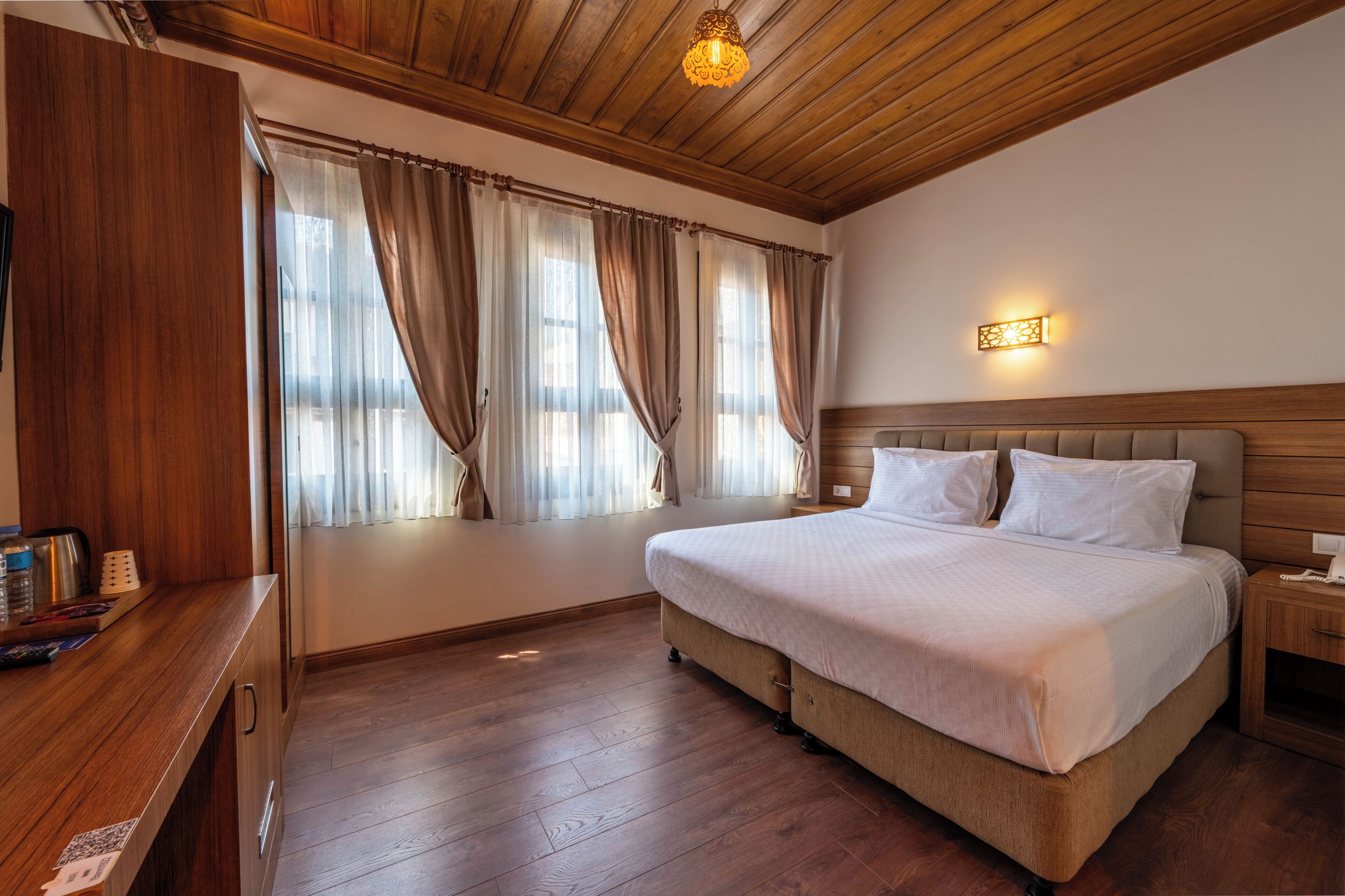 Un dormitorio con techo de madera, una cama con ropa de cama blanca, una mesita de noche y un velador.