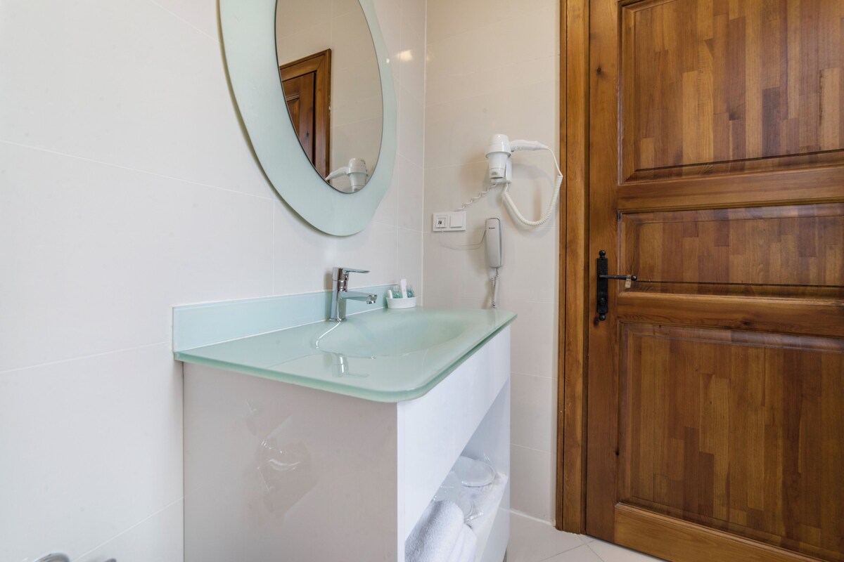 A bathroom with a glass sink, a wooden door, and a hairdryer on the wall.