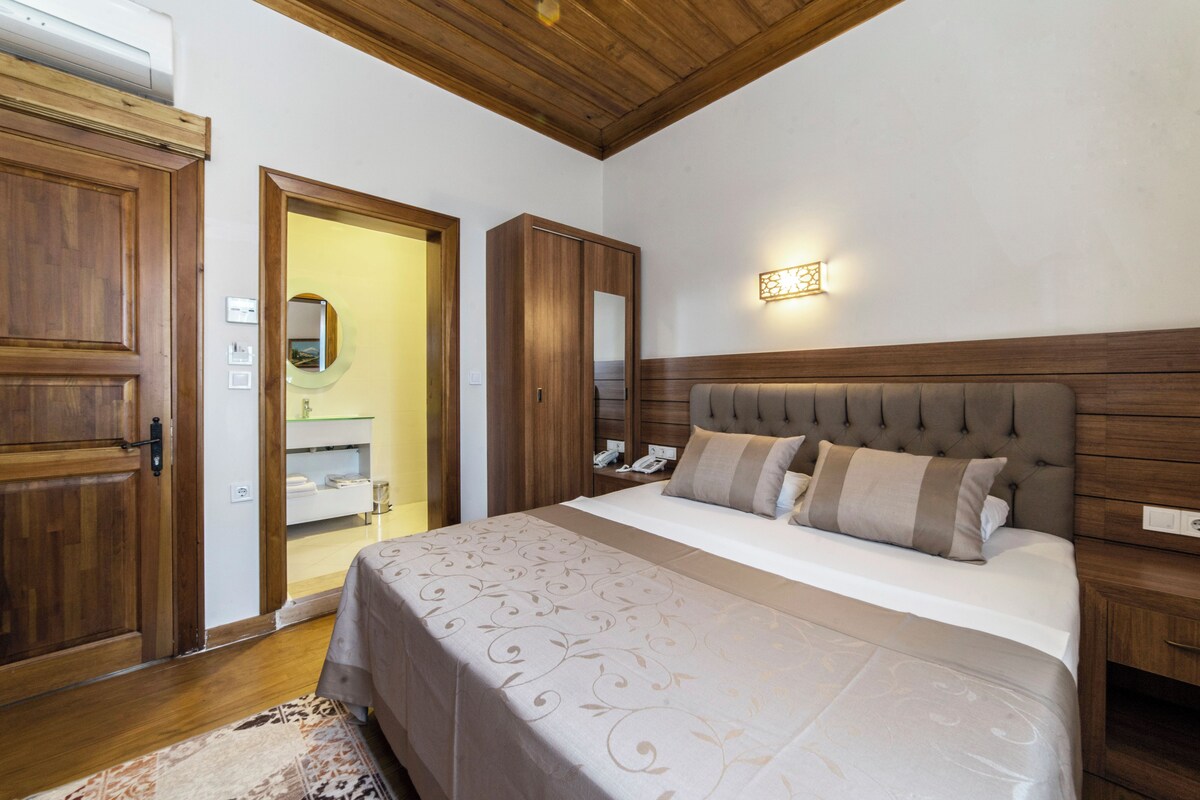 A bedroom with a large bed, wooden wardrobe, and a mirror.