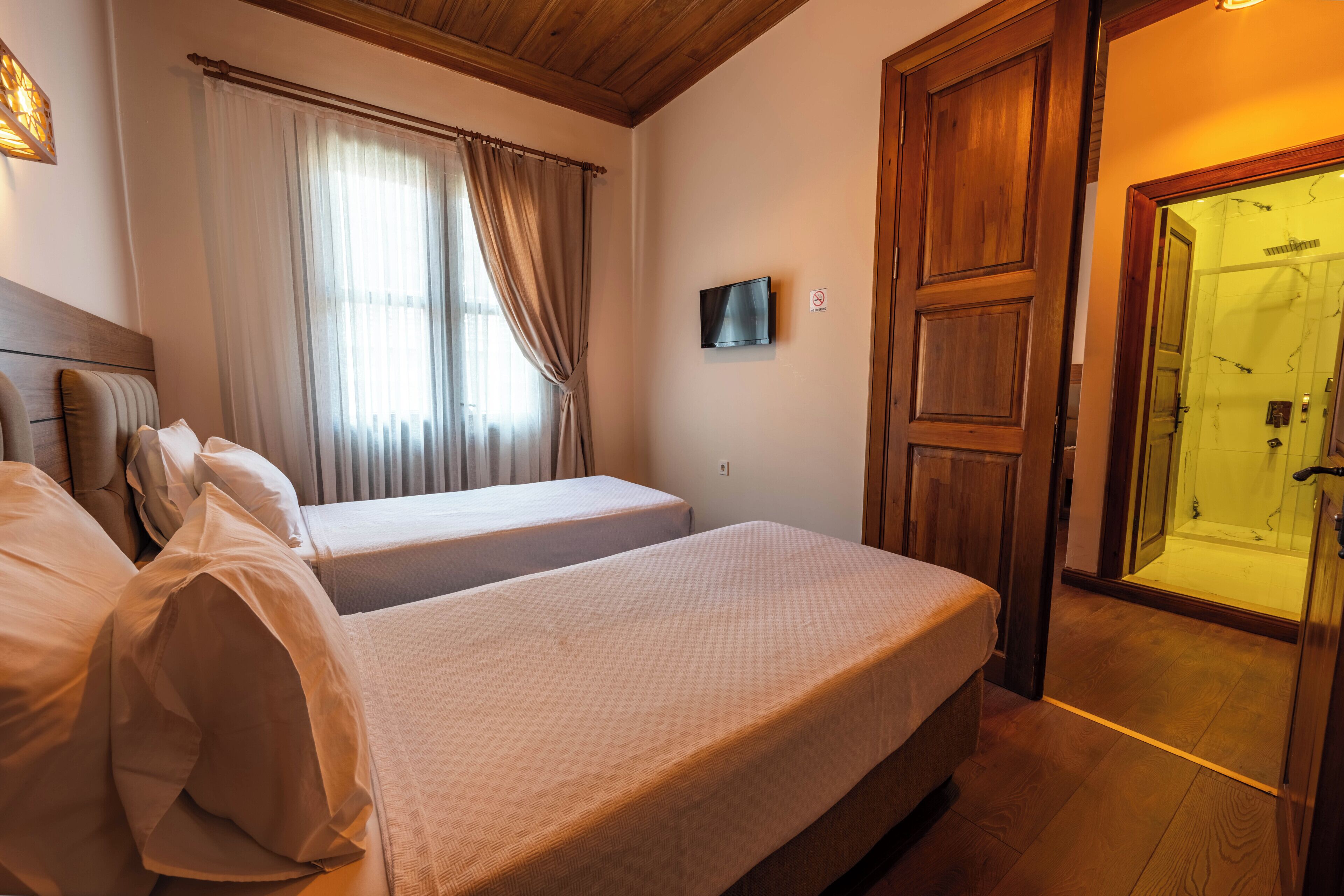 Een slaapkamer met twee bedden, een televisie en een houten deur die naar een badkamer leidt.