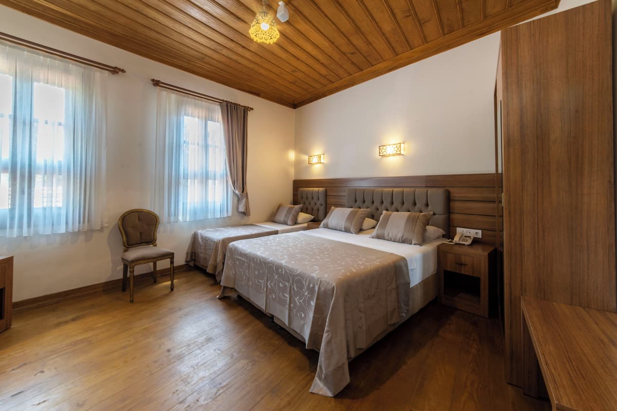 A bedroom with two beds, wooden flooring, a chair, bedside tables, and a ceiling light fixture.
