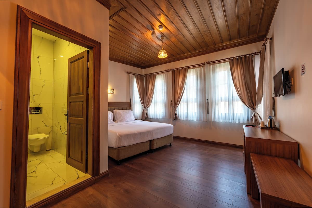 A room with a wooden ceiling, a bed, a desk, and a bathroom with a marble floor.