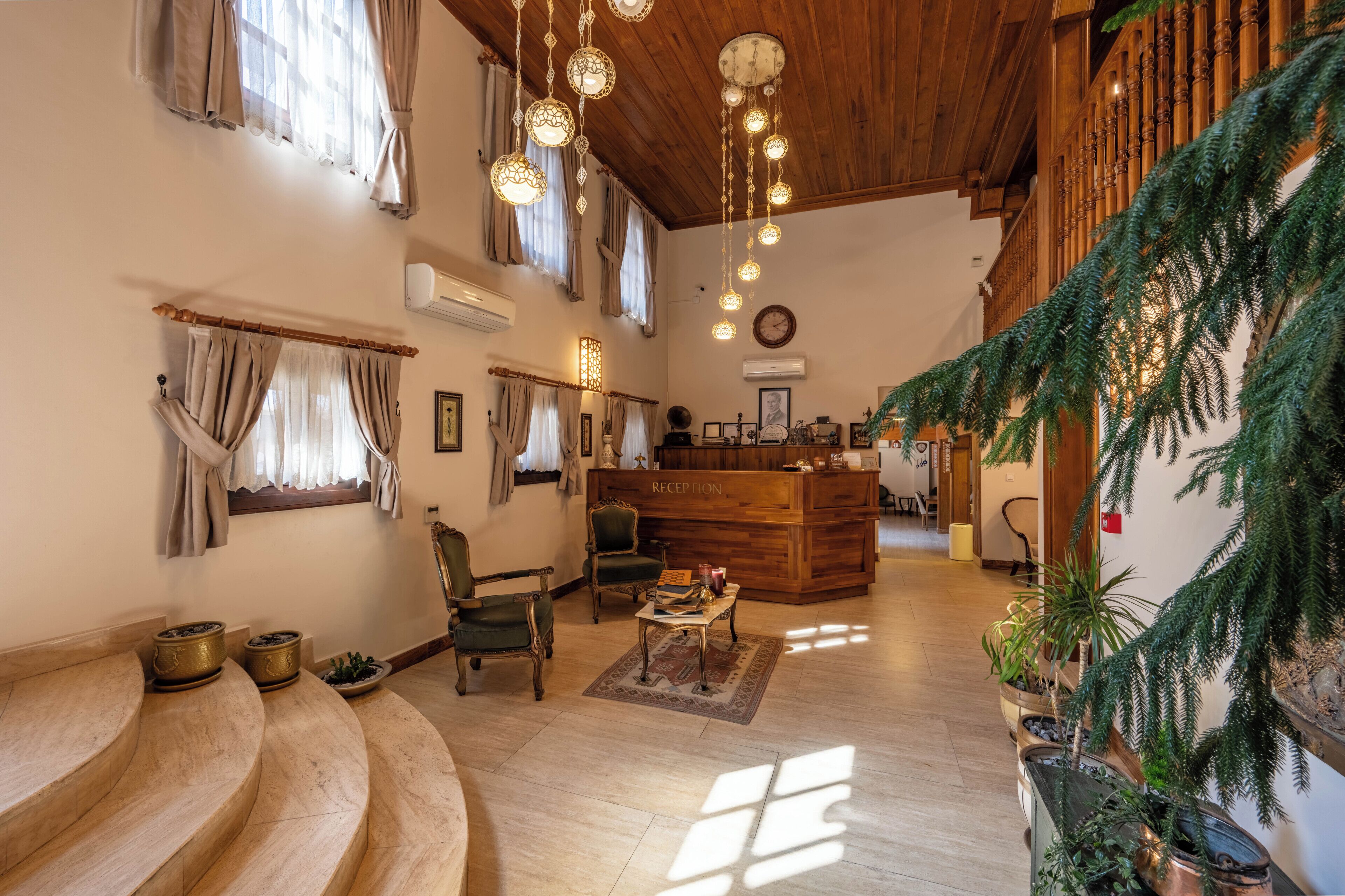 A spacious lobby with a reception desk, wooden flooring, and large windows with curtains.