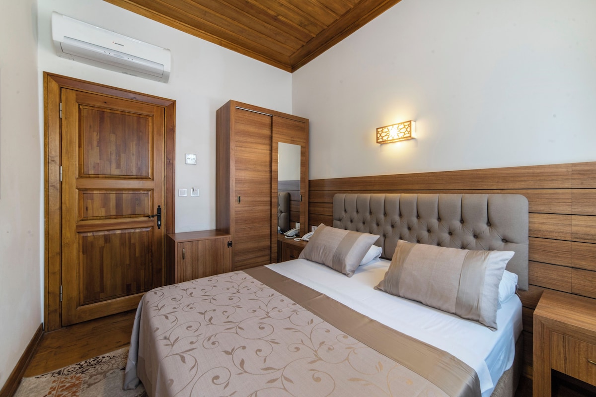 Un dormitorio con cabecera de madera, cama con ropa de cama estampada, un armario, un espejo y una lámpara fijada a la pared.