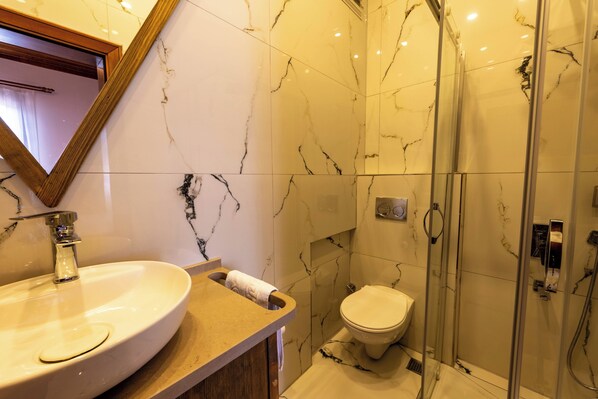Un baño con lavamanos de mármol, inodoro y ducha con mampara de vidrio.
