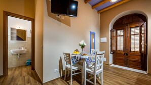 Uma sala de jantar com mesa posta para dois, uma TV fixada na parede e uma porta de madeira com portões.