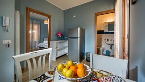 Uma área de refeições com uma mesa posta para dois, um refrigerador e vista para um banheiro.