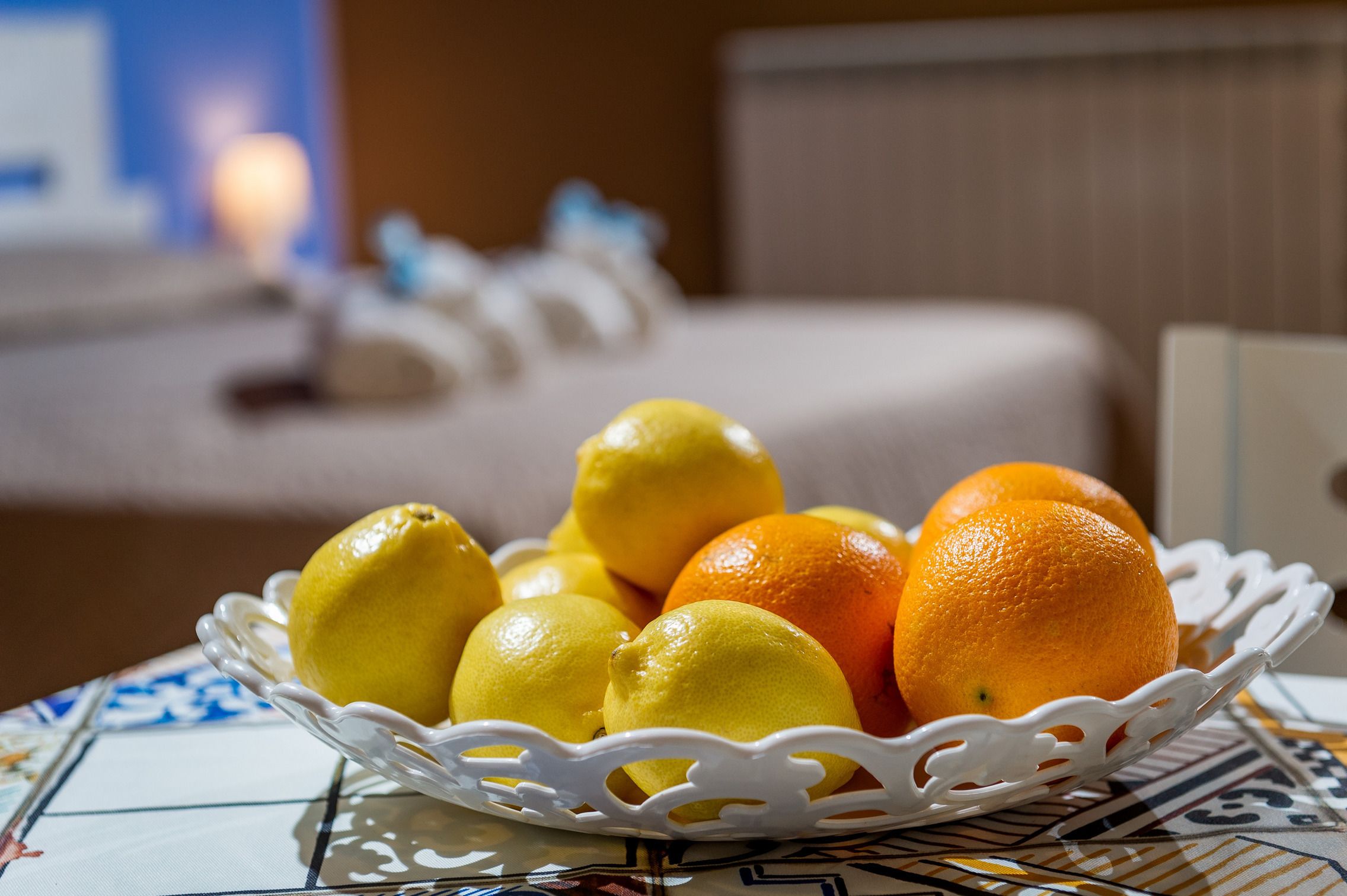 A white basket filled with lemons and oranges on a table with a patterned tablecloth.