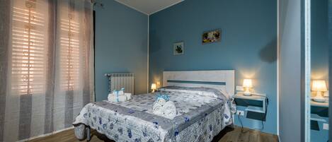 A bedroom with a bed, a bedside table with a lamp, a radiator, and a window with curtains.