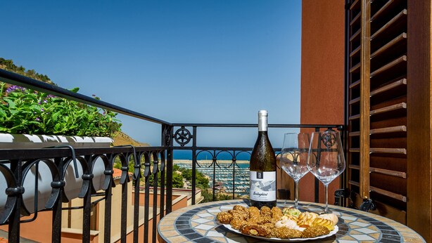 Uma mesa com uma garrafa de vinho e copos, um prato de comida e vista para o mar.