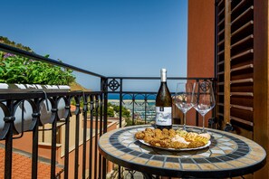 Une table avec une bouteille de vin et des verres, une assiette de nourriture et une vue sur la mer.