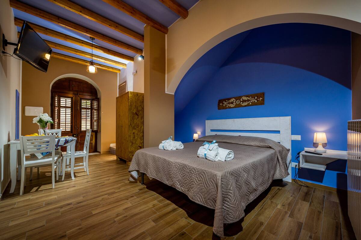 Een hotelkamer met een bed, een bureau met stoelen, een televisie en een blauwe accentmuur.