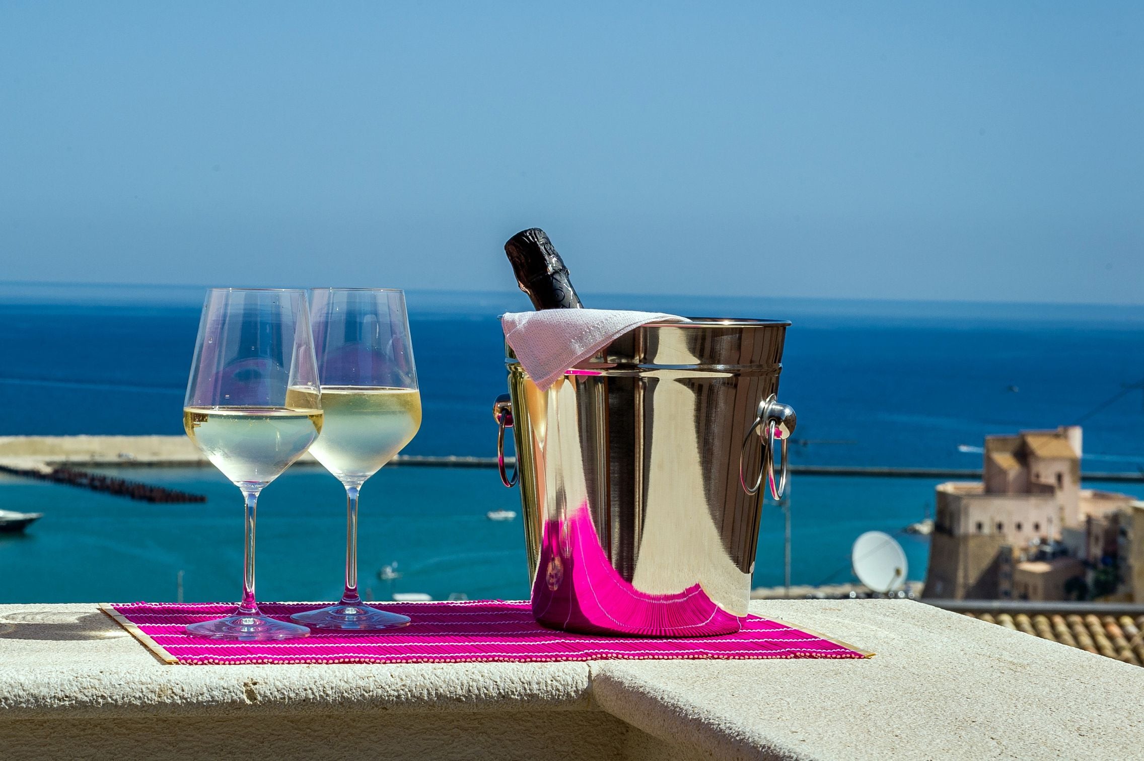 Deux verres de vin blanc sur un balcon, avec un seau en métal et un torchon rose.