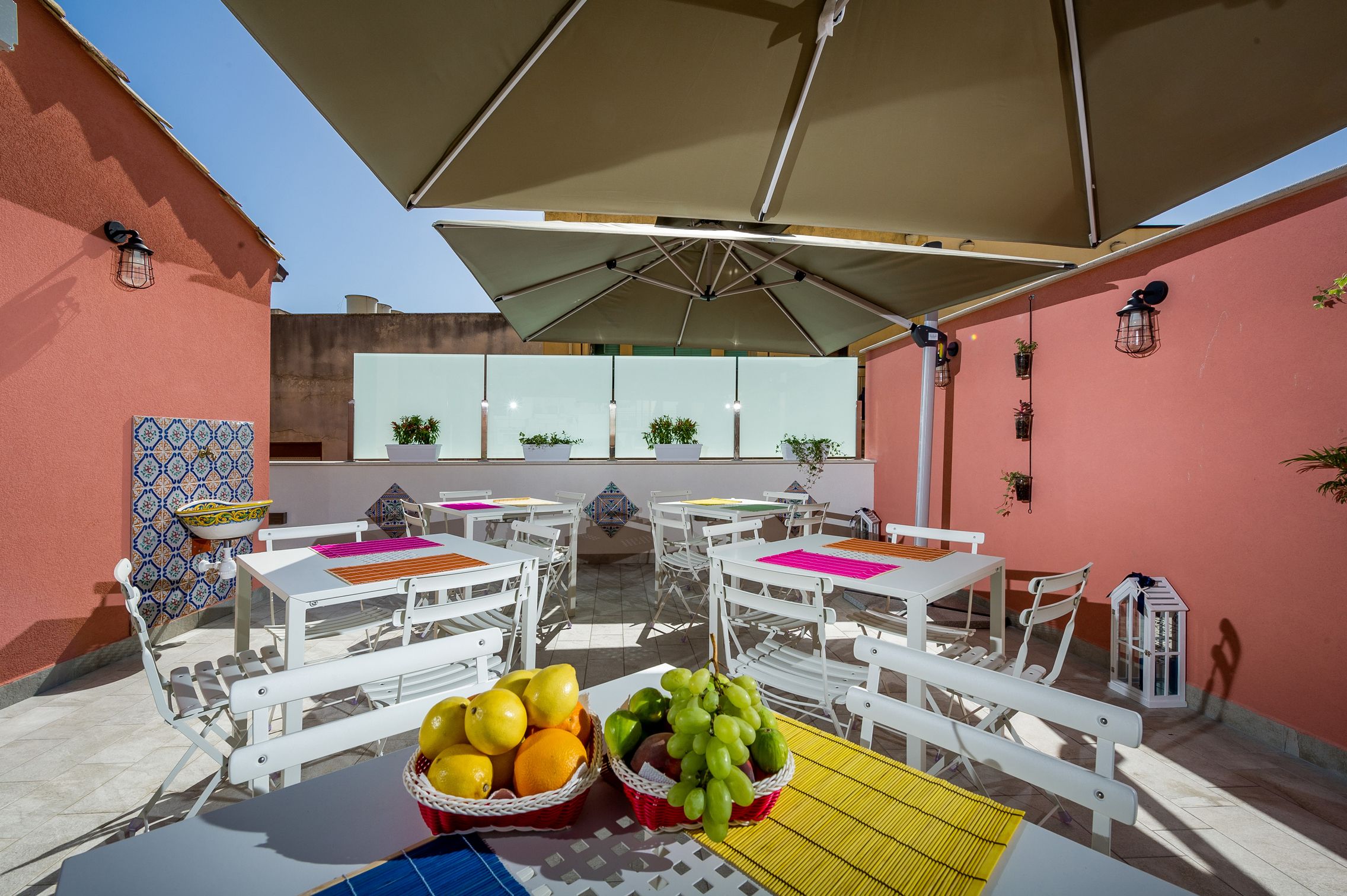 An outdoor patio with white tables and chairs, a large umbrella, and baskets of fruit.