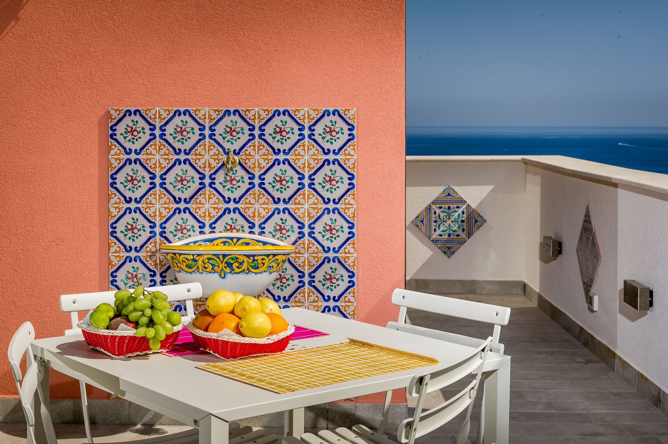 Una mesa con cestas de fruta y una pared decorada con azulejos, con vista al mar.