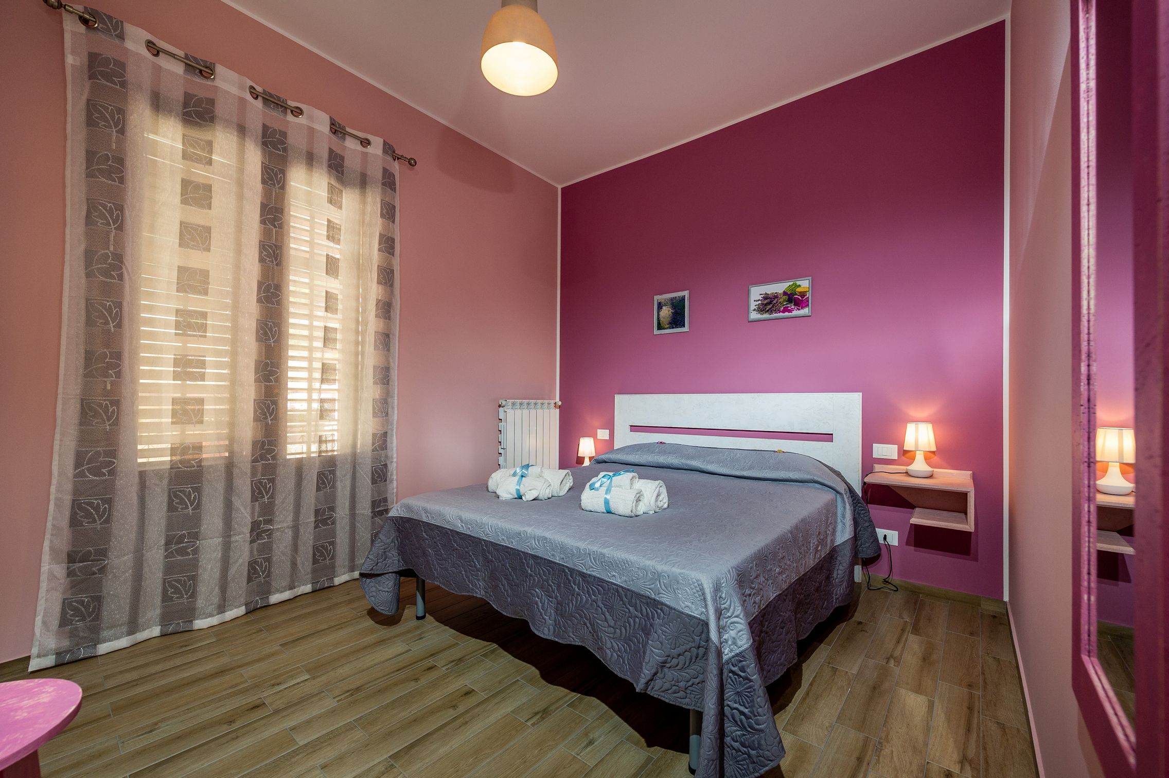 Un dormitorio con cama, una mesita de noche con lámpara, una ventana con cortinas y un radiador.