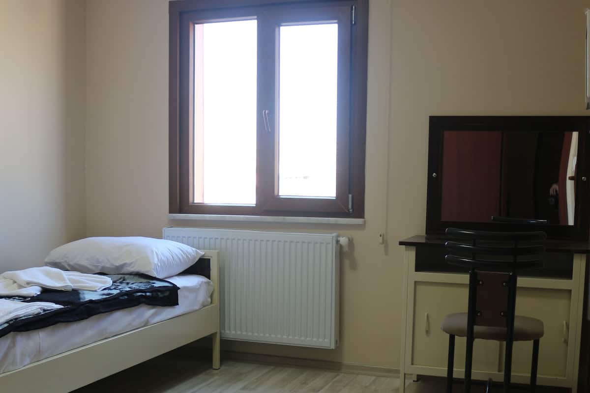 A small room with a single bed, a desk, a chair, and a window.