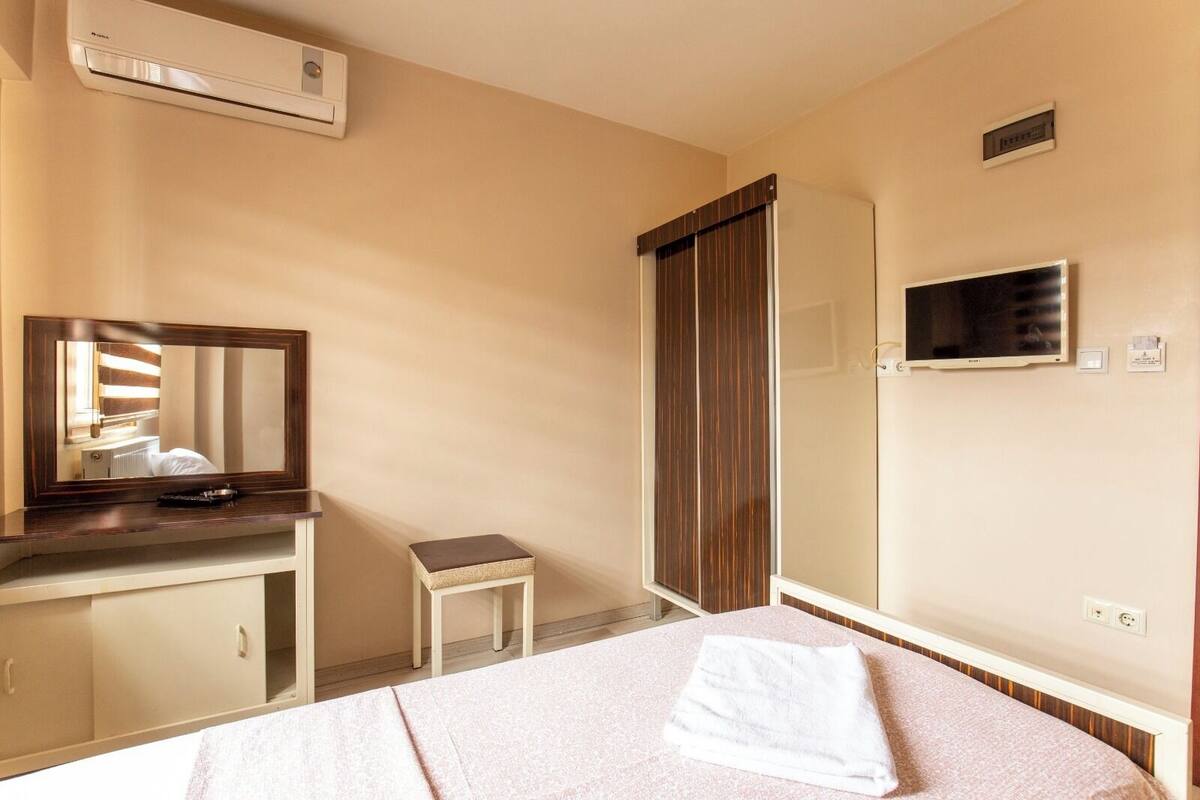 A hotel room with a bed, a small bedside table, a mirror, a TV, and a wardrobe.