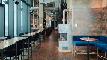 A modern restaurant with long communal tables, a blue cushioned seating area, and a fireplace.