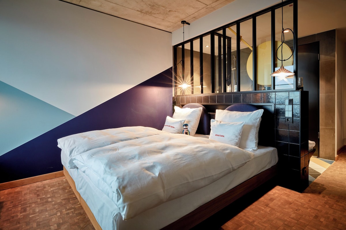Une chambre d’hôtel moderne dotée d’un grand lit, d’une tête de lit en bois et d’un décor mural géométrique original.