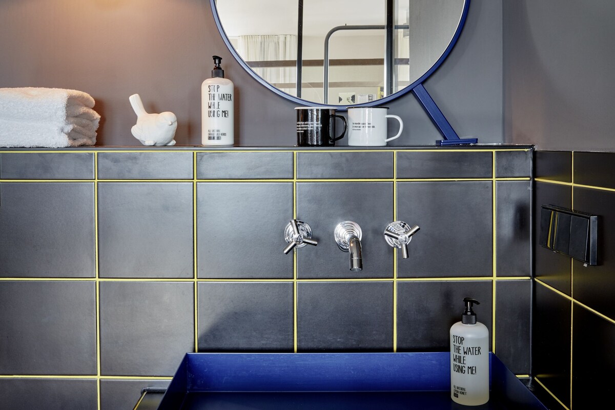 Une salle de bain avec un lavabo bleu, un miroir rond et un porte-serviettes.