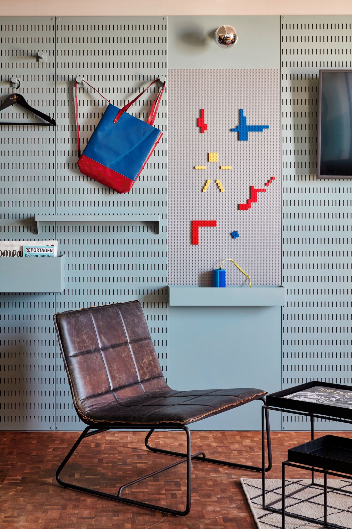 A room with a pegboard wall, a leather chair, a small table, and a hanging bag.
