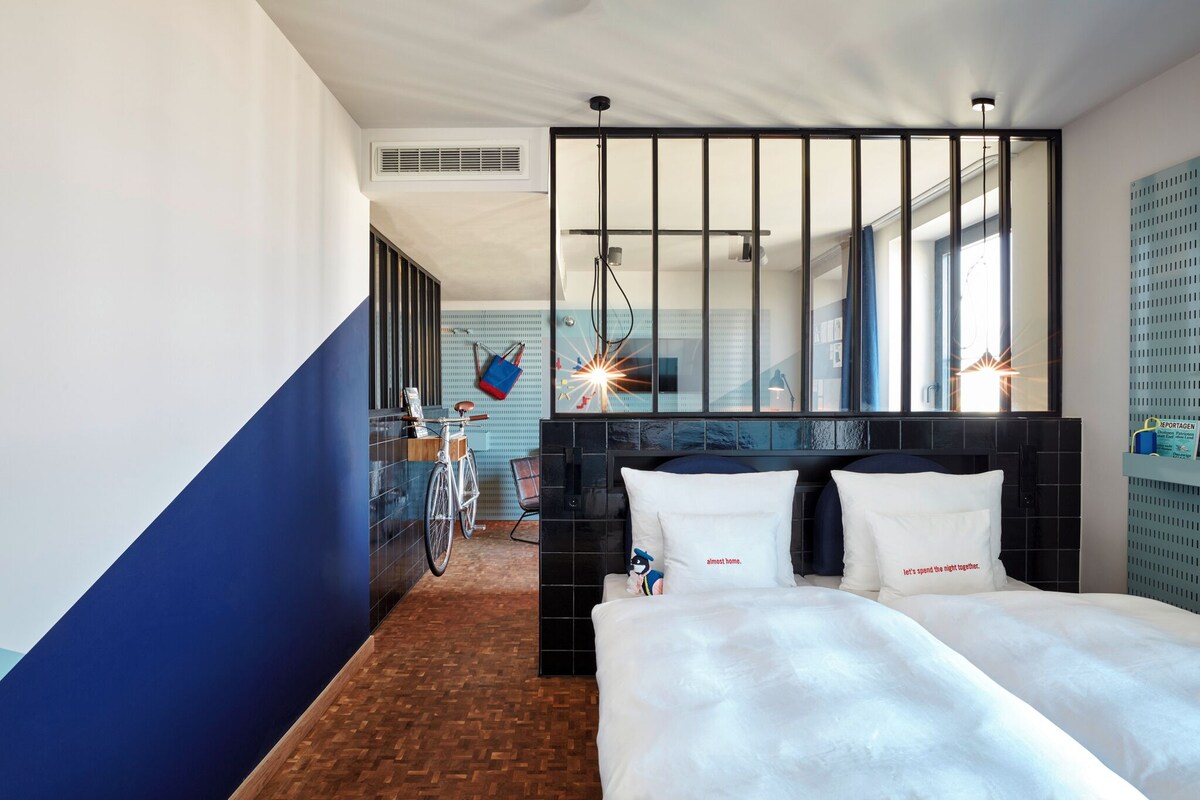 Une chambre d’hôtel avec un grand lit, un vélo en arrière-plan et une vue sur la ville.