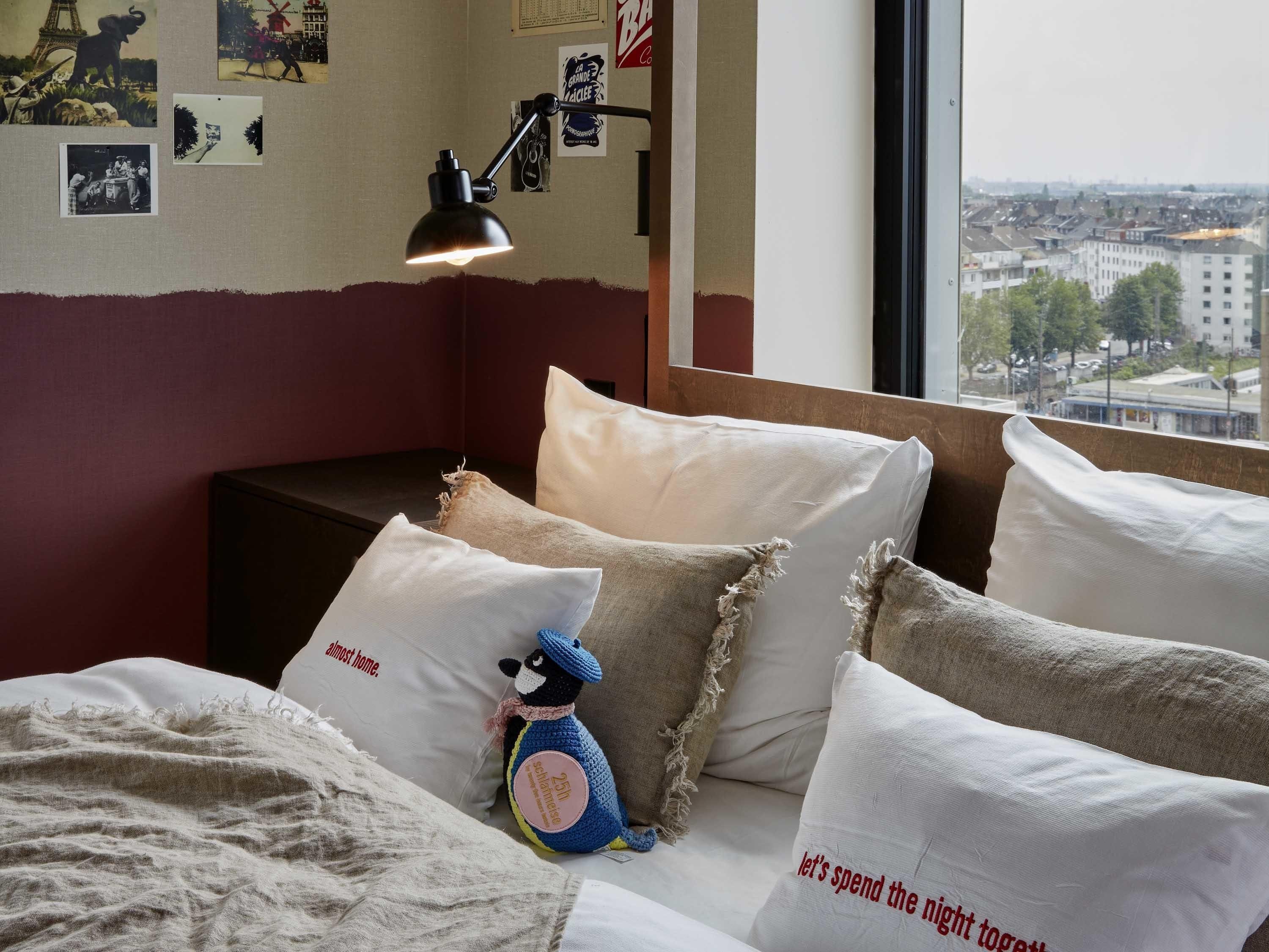 Une chambre à coucher avec un lit, des oreillers, une lampe et une vue sur le paysage urbain par la fenêtre.