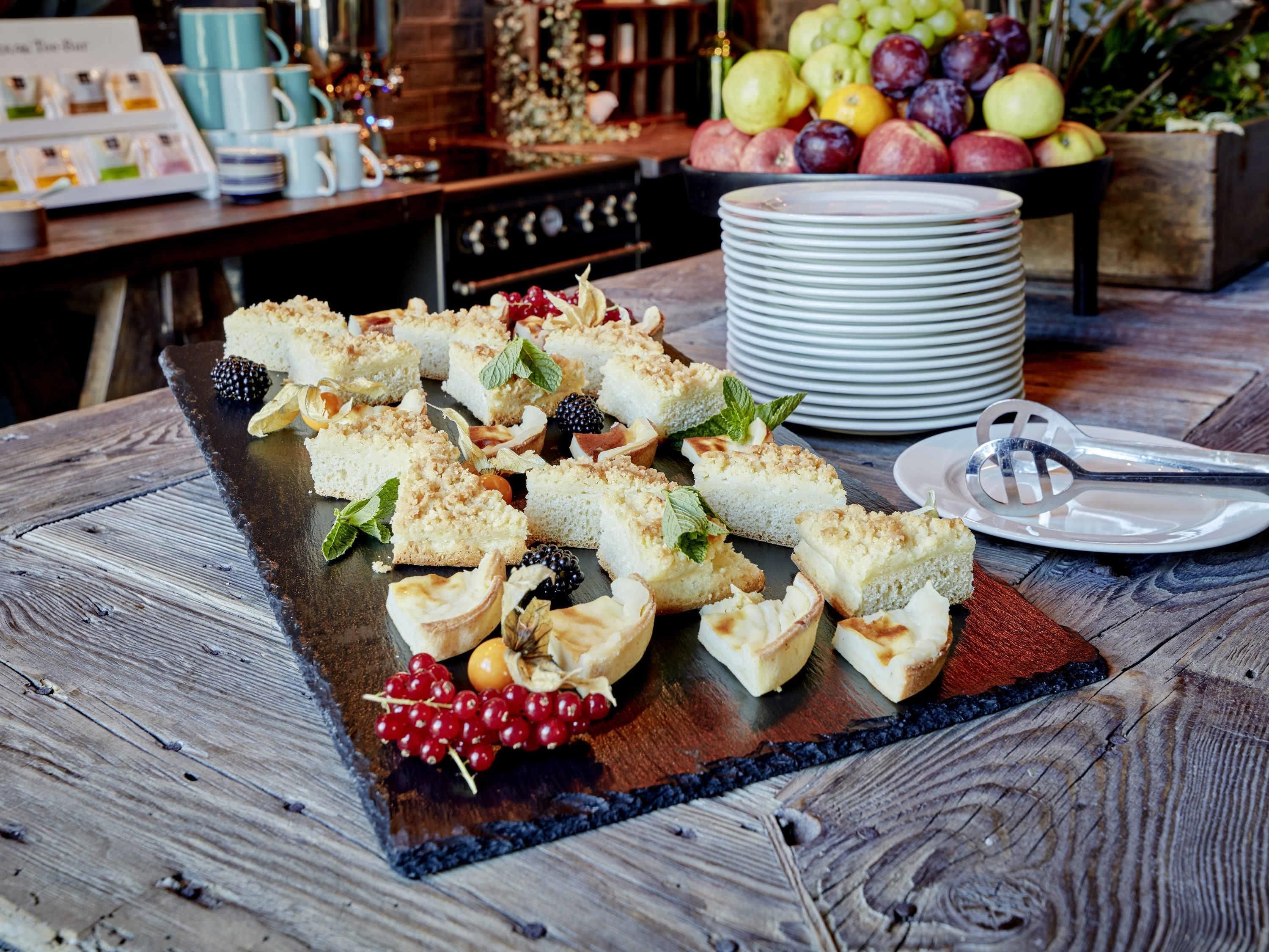 A wooden table with a slate serving tray holding several small, crumbly pastries garnished with mint leaves and berries.