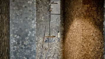 Doccia con soffione manuale e flessibile, su un fondo di parete in mosaico.