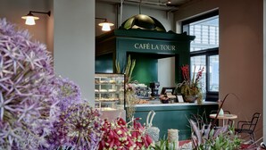 Interior de una cafetería con un mostrador verde, una vitrina con pasteles y vistas al exterior.