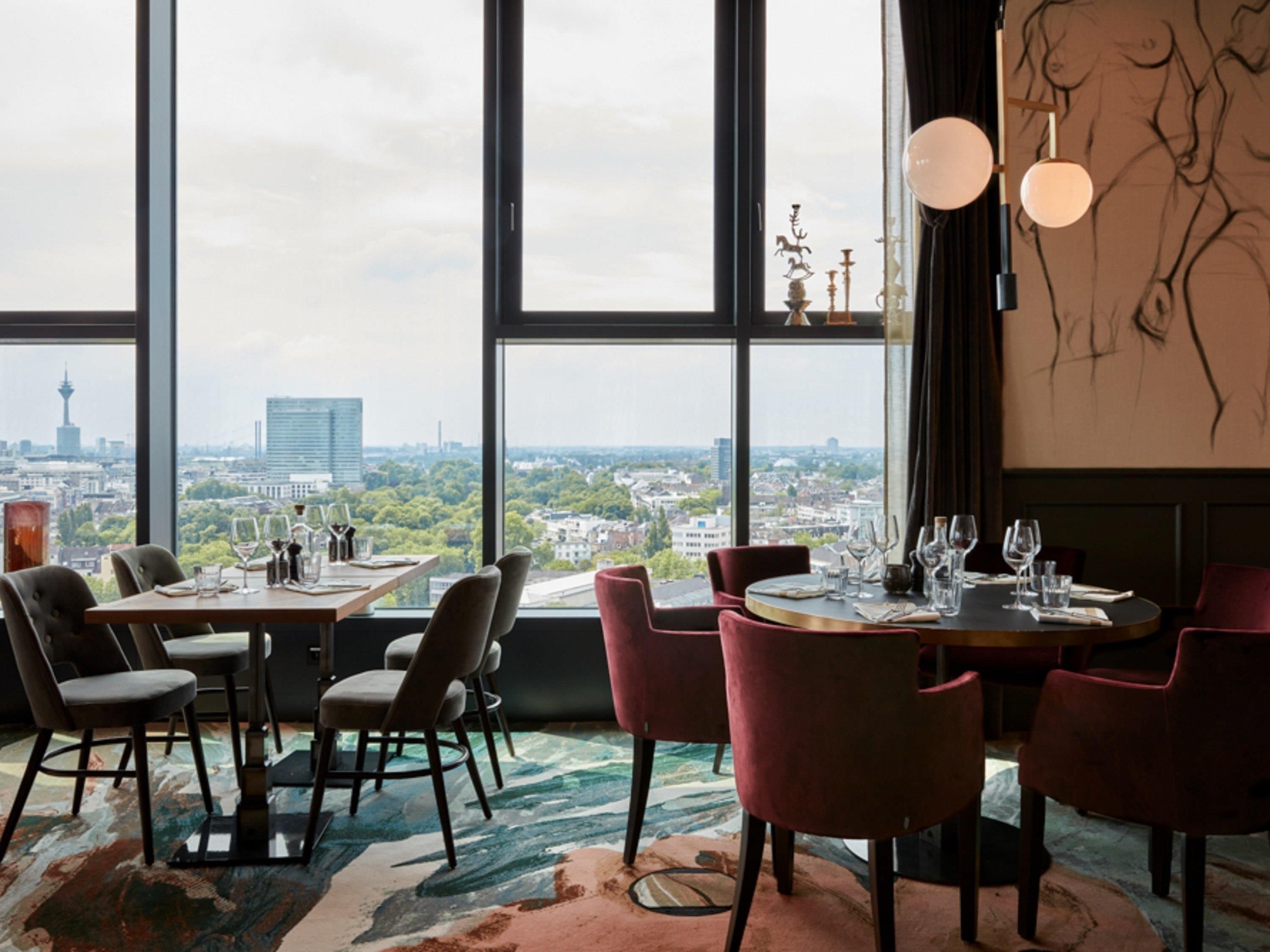 A dining area with a city view, tables set with wine glasses, and a large window.