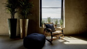 Una habitación con un ventanal grande, una silla de mimbre y dos plantas grandes en macetas.
