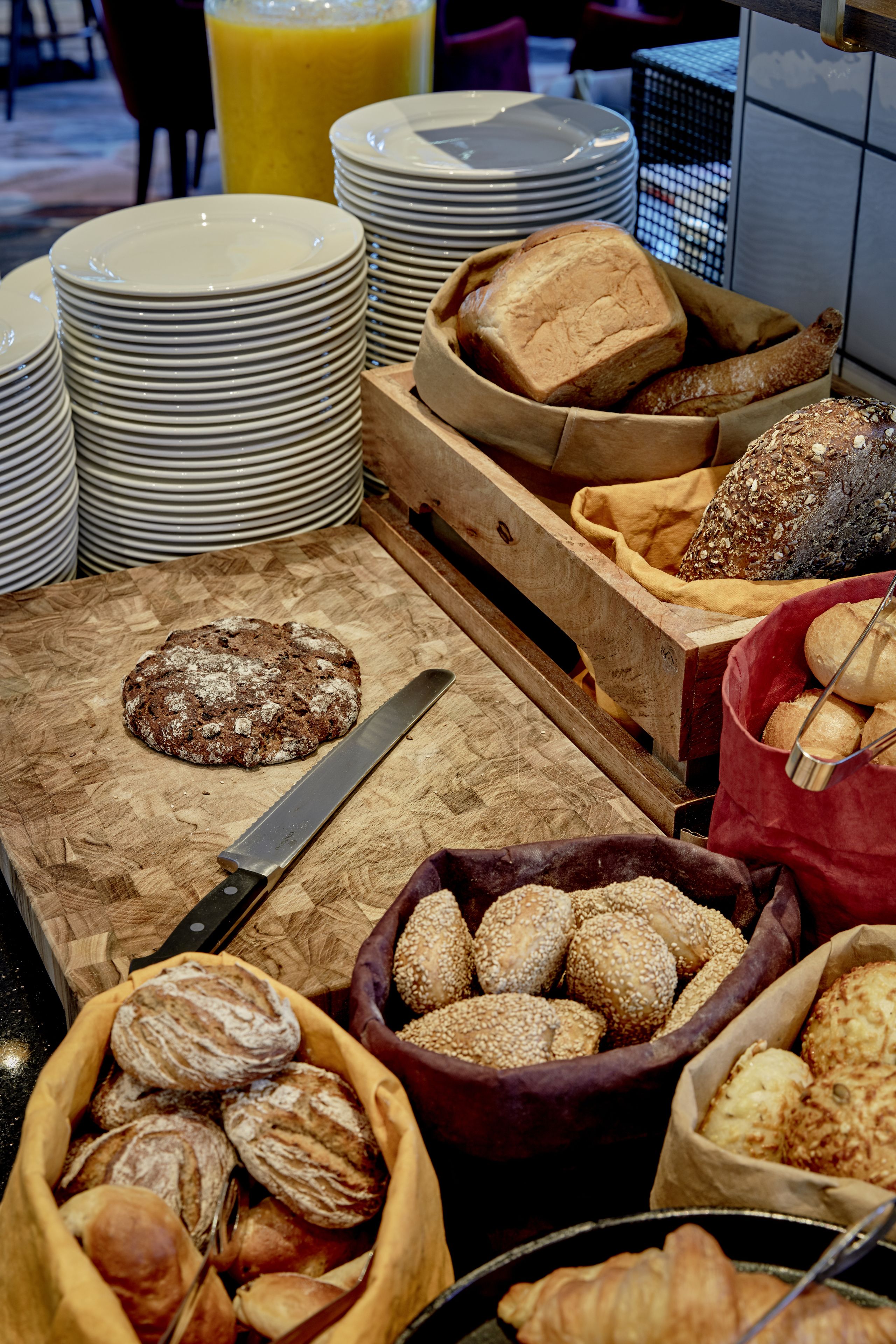 Um buffet de café da manhã com diversos pães, croissants e uma faca em tábua de corte.