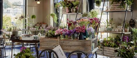 En blomsterbutik med mange planter og blomster udstillet på hylder og i en tralle.