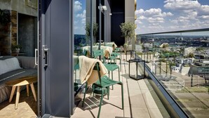 Un balcón moderno con sillas verdes y un sofá, una puerta de cristal y vistas a la ciudad.