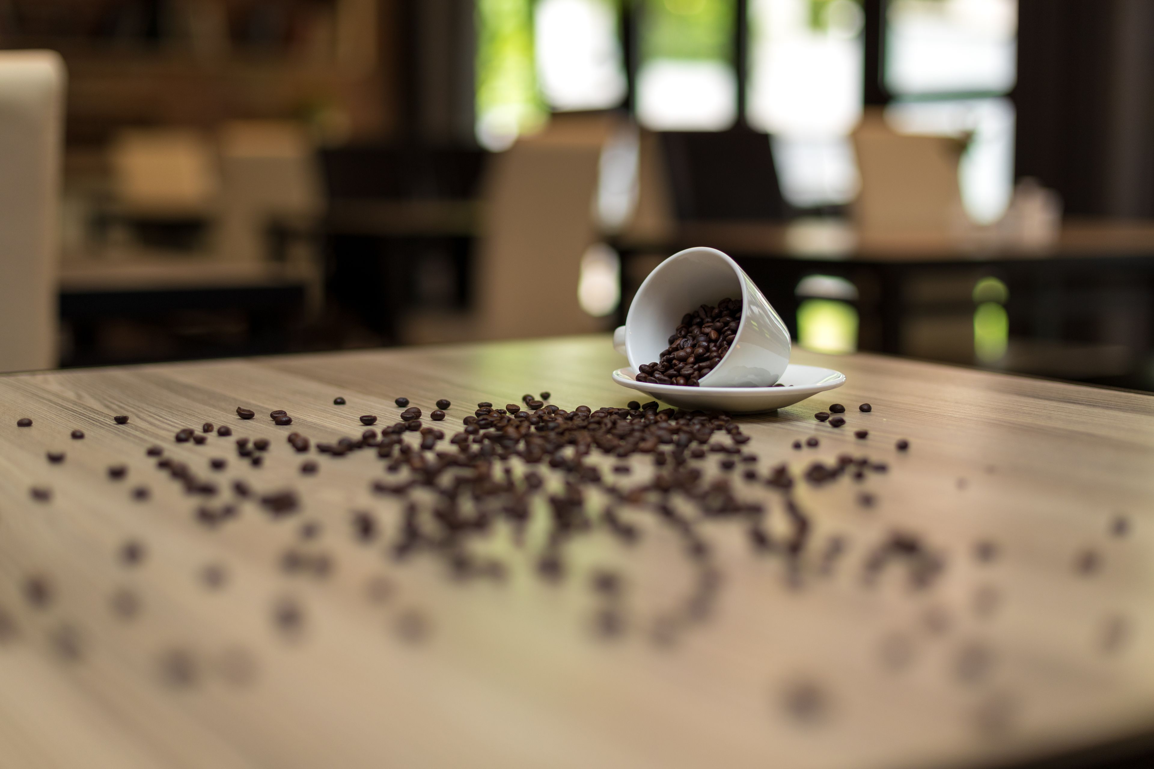 Una taza blanca volcada sobre una mesa de madera, con granos de café esparcidos.